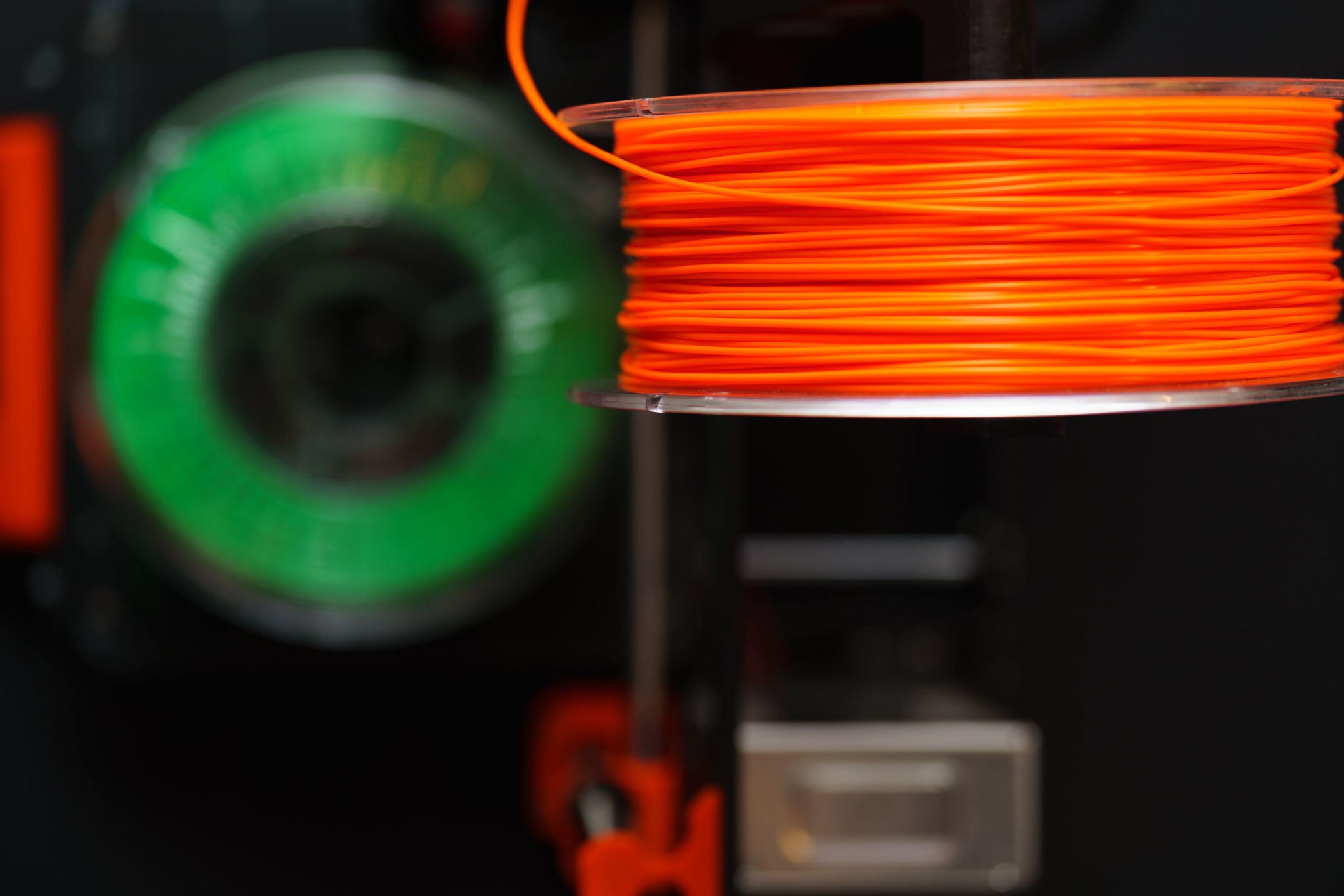 Orange 3D printing filament spool with a green spool in the background